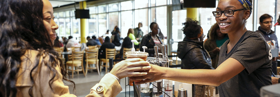 Female students hands another female student an iced coffee