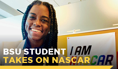 african american student smiling in front of rainbow colored sign that says i am nascar text says bsu student takes on nascar