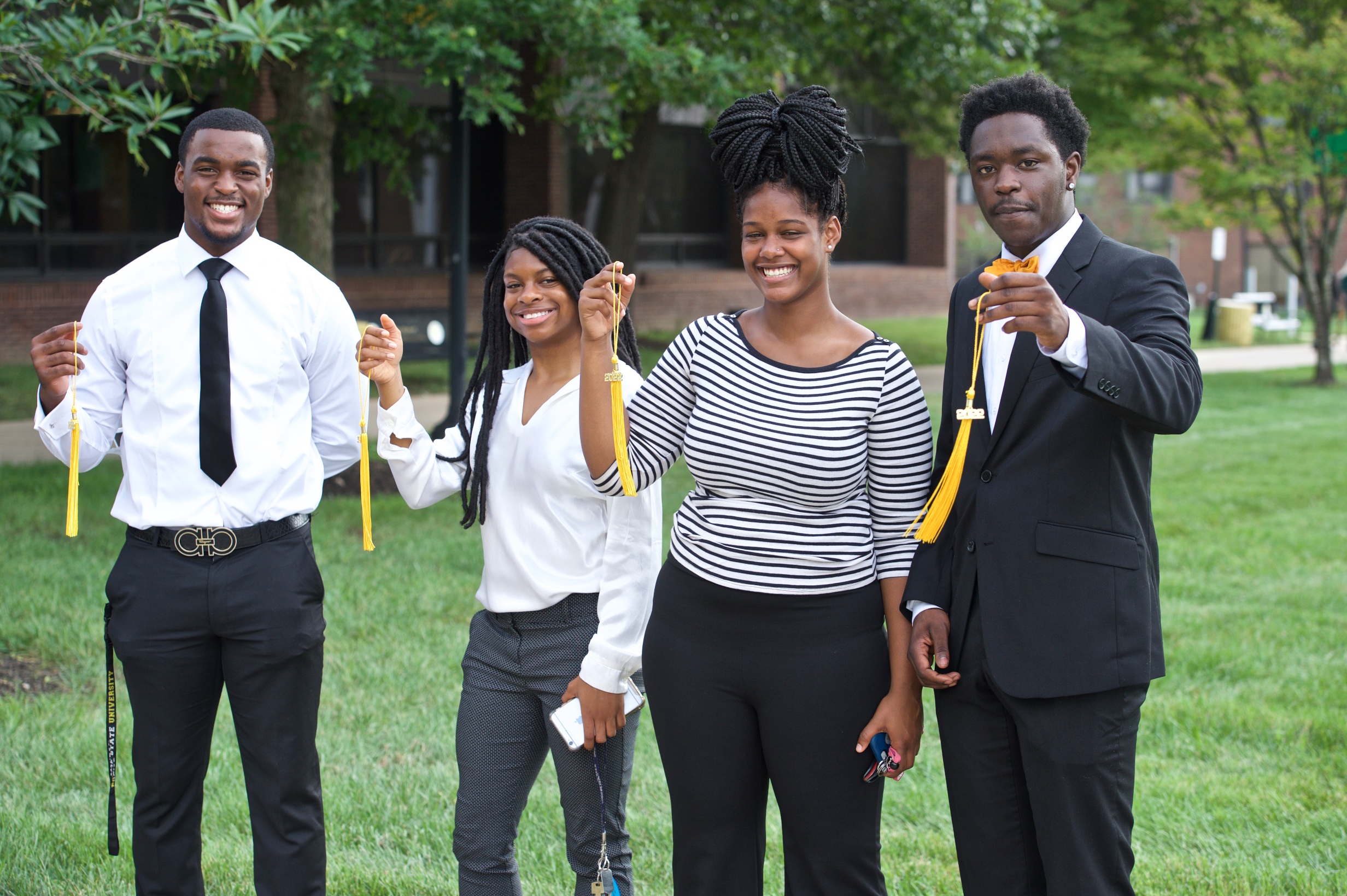 Two male students and two female students stand together, holding gold tassels